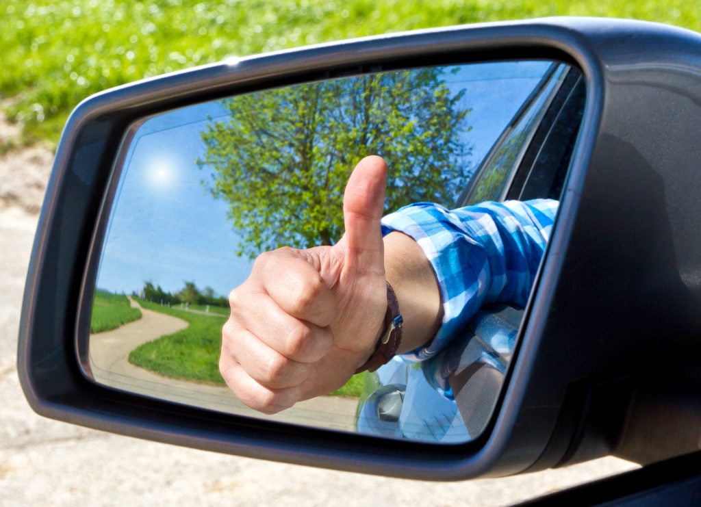 Car driver with thumb up in a side mirror