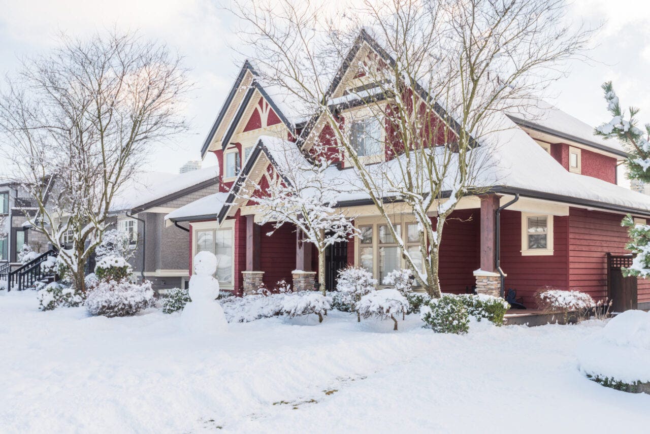 The exterior of a large house and front garden covered in snow.