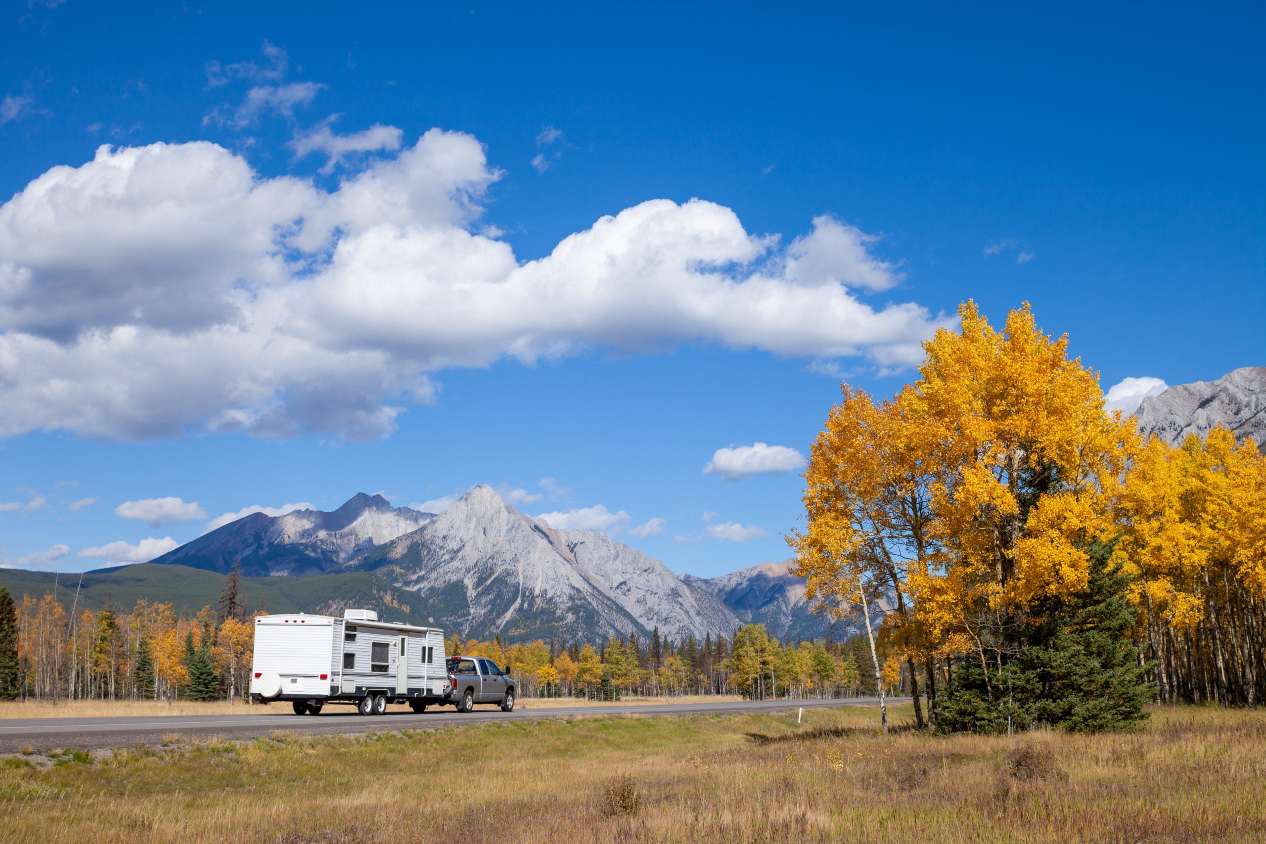 Truck and trailer heading west on the highway towards the mountains in fall in Kananaskis Country.
