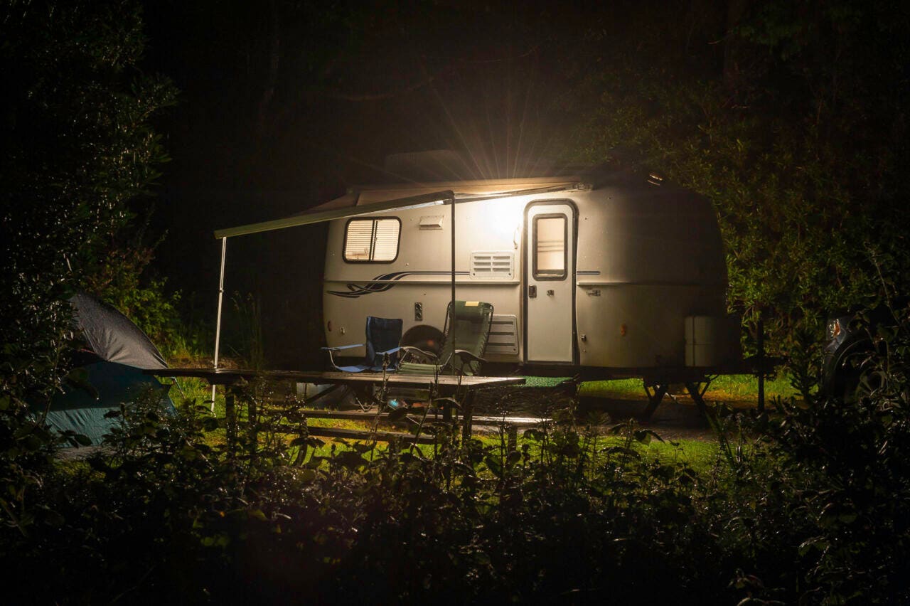 Compact travel trailer glowing with warm light through windows in a forest RV park in the Pacific Northwest of the USA. ProPhoto RGB profile for maximum colour fidelity and gamut.