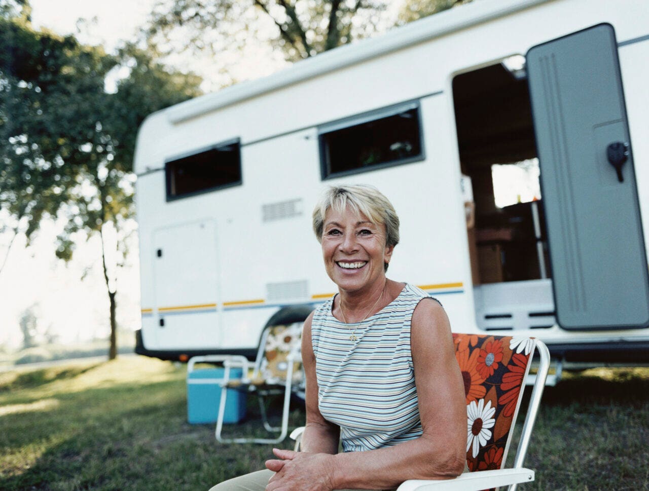 Mature Woman Sits in a Deckchair in Front of a Caravan, Smiling and Looking at the Camera