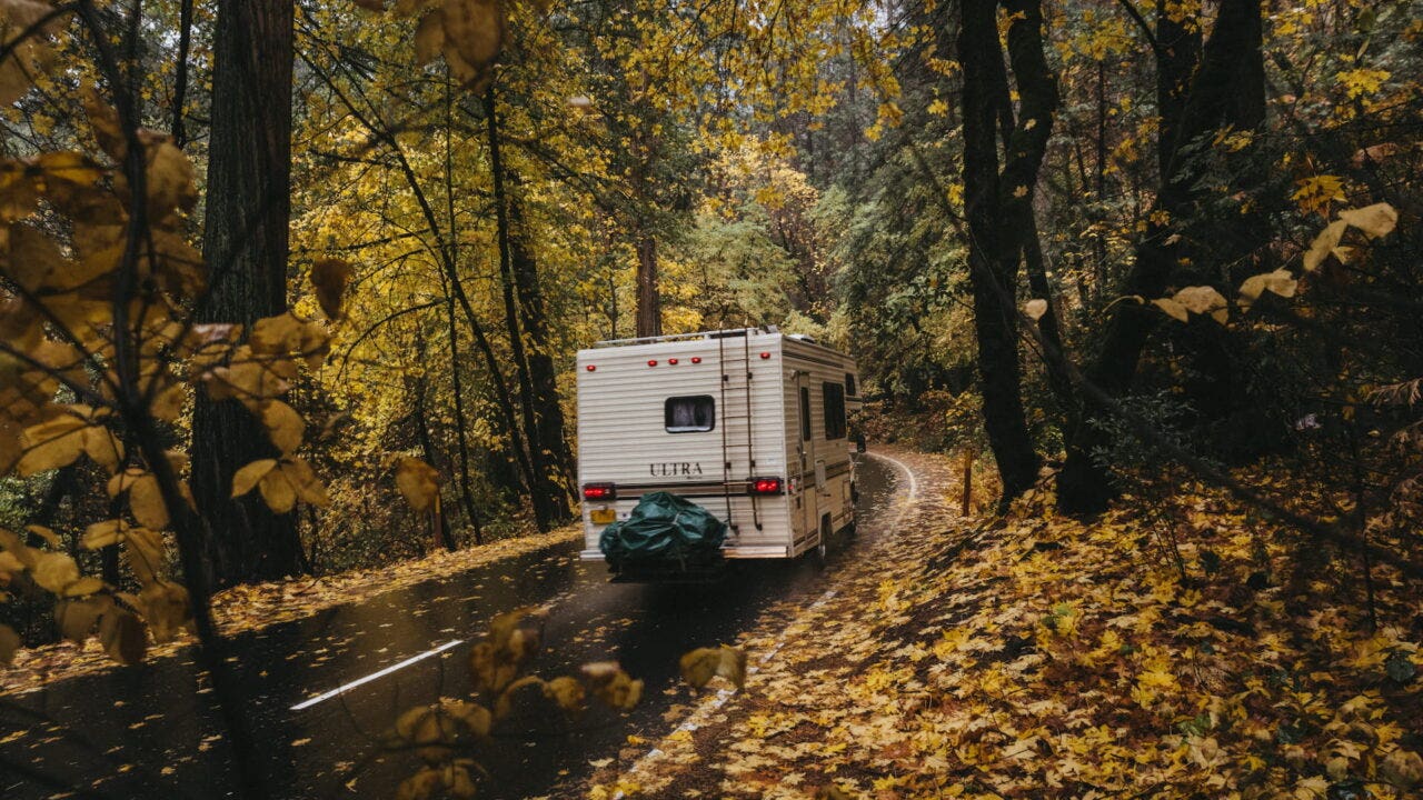 A motorhome driving through the rain on a windy forest road in autumn.