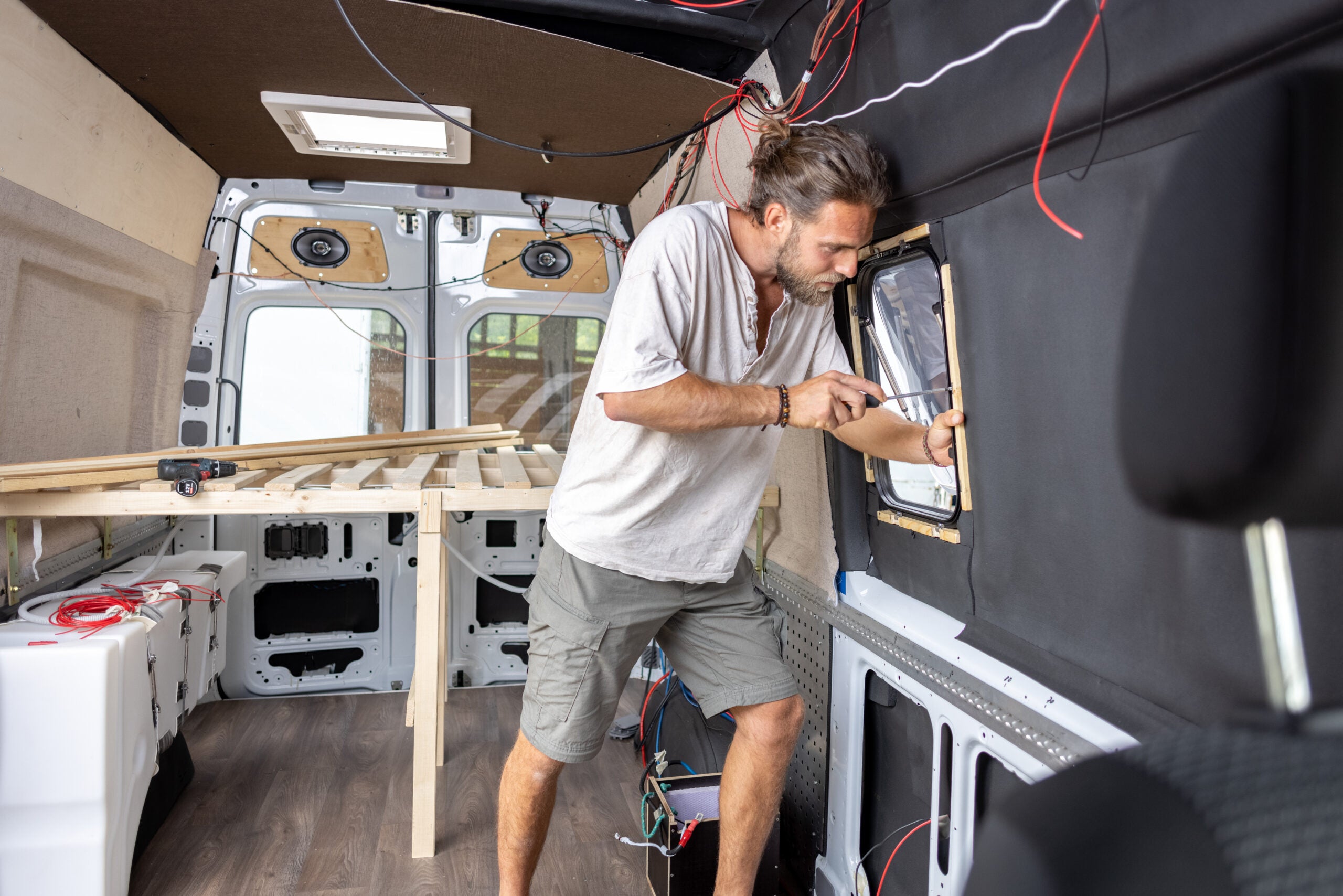 Interior view. A man is converting a van into a caravan. He is tightening a screw in the side window.