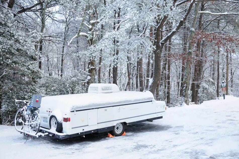 A snow-covered tent trailer in a forest.