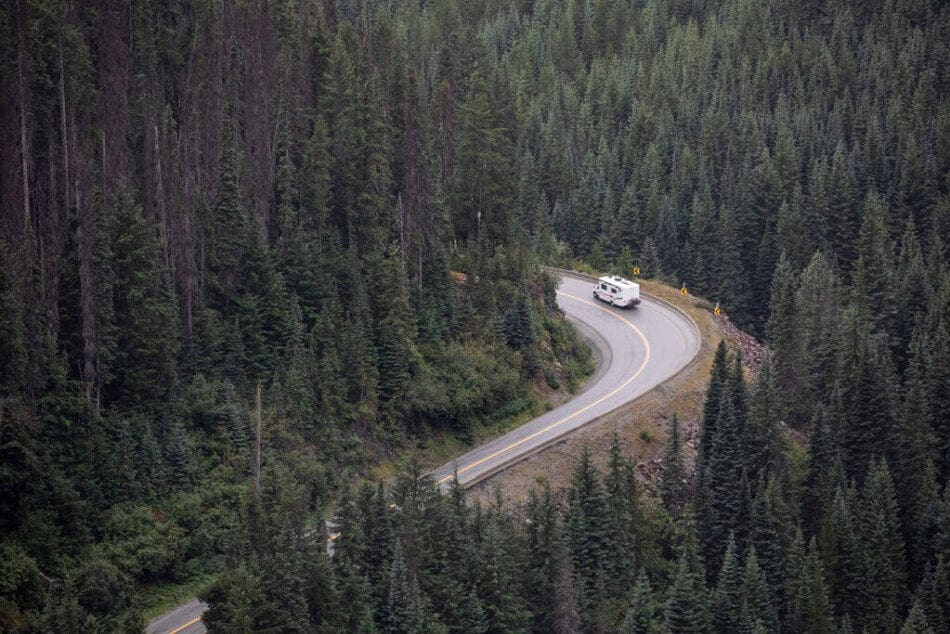 A motorhome driving around a bend through a forest in BC.