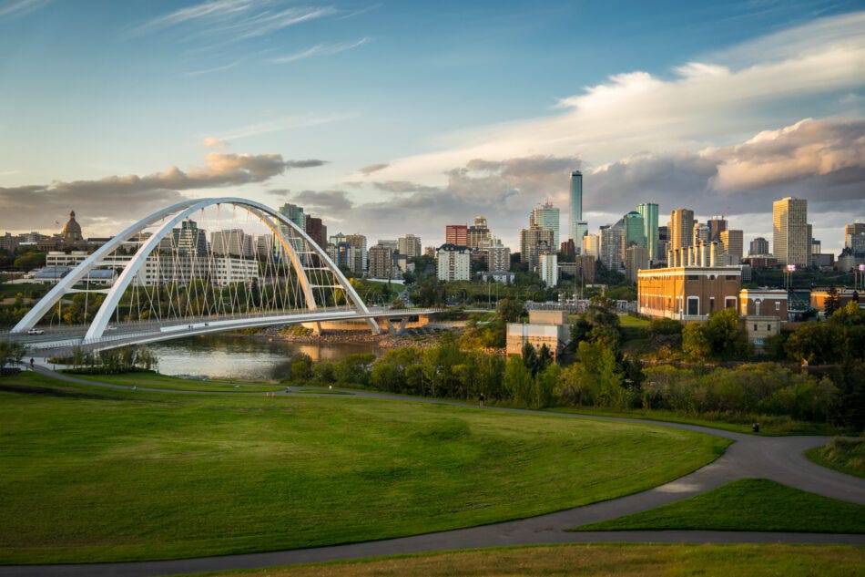 View of the Walterdale suspension bridge and Saskatchewan River in Edmonton, Alberta Canada at dusk. With a field and bike path in the foreground and a view of the Edmonton skyline in the background.