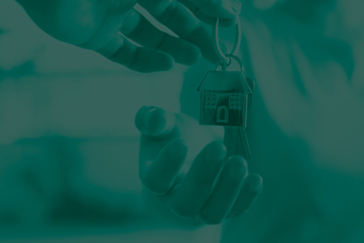 Hand giving a key with a house keychain to another hand