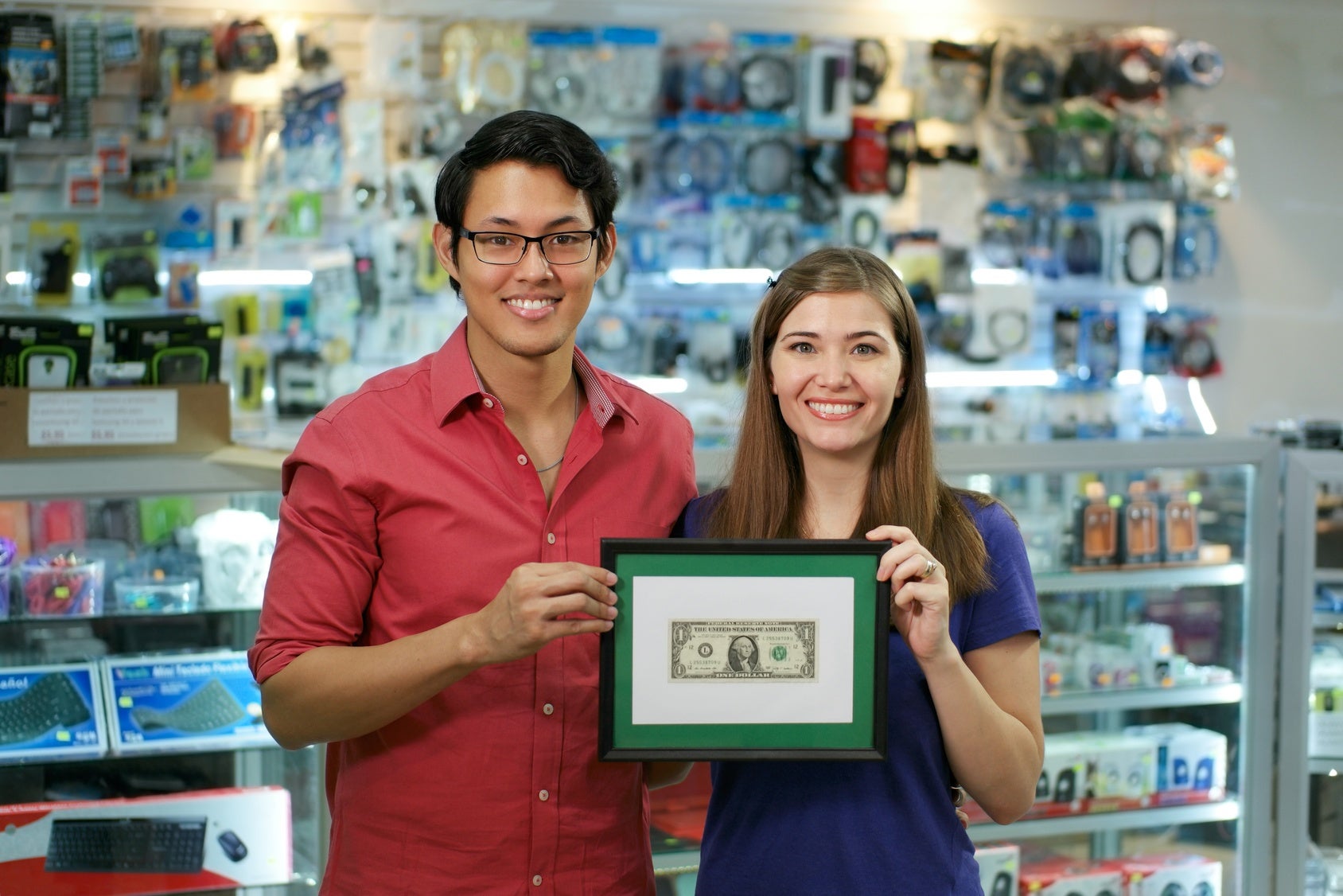 Young couple holding up a framed dollar bill and smiling in their business