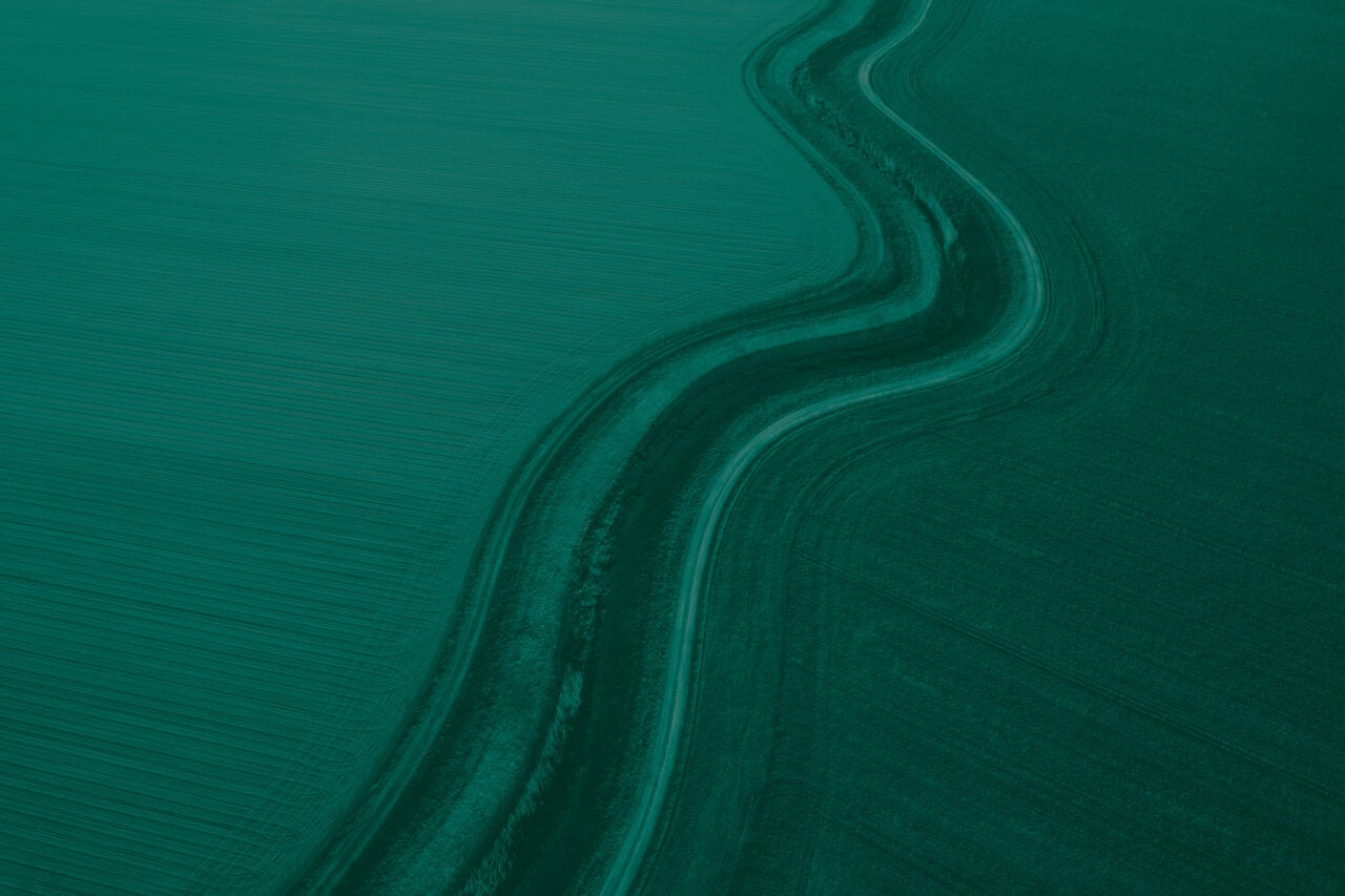 Aerial view of winding road with forest on one size and farm field on the other side