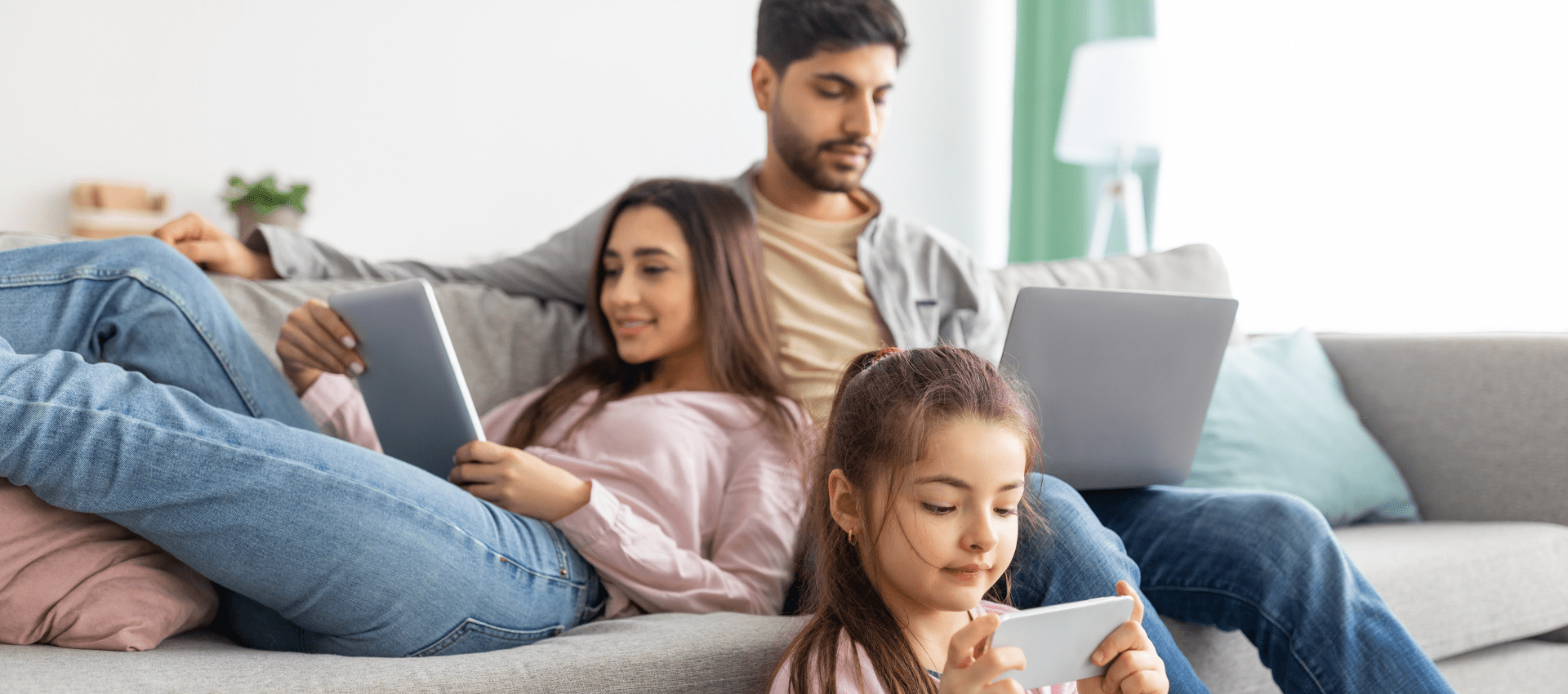 Young family sitting in their living room looking at tabs and laptops