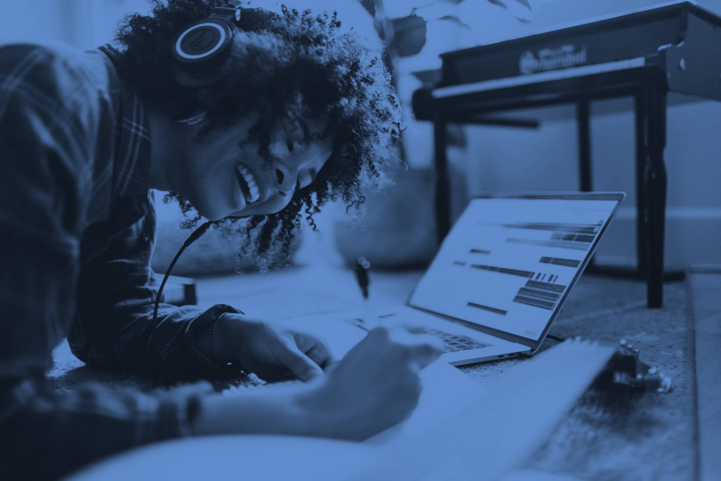 Happy woman writing at desk with laptop next to her and headphones on